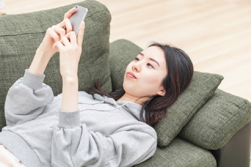 ソファーで携帯を触る女性の写真